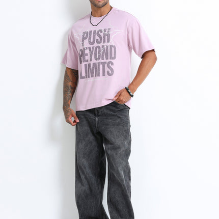 Man wearing a pink t-shirt with text and dark jeans on a white background