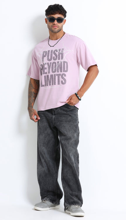 Man wearing a pink t-shirt with text and dark jeans on a white background