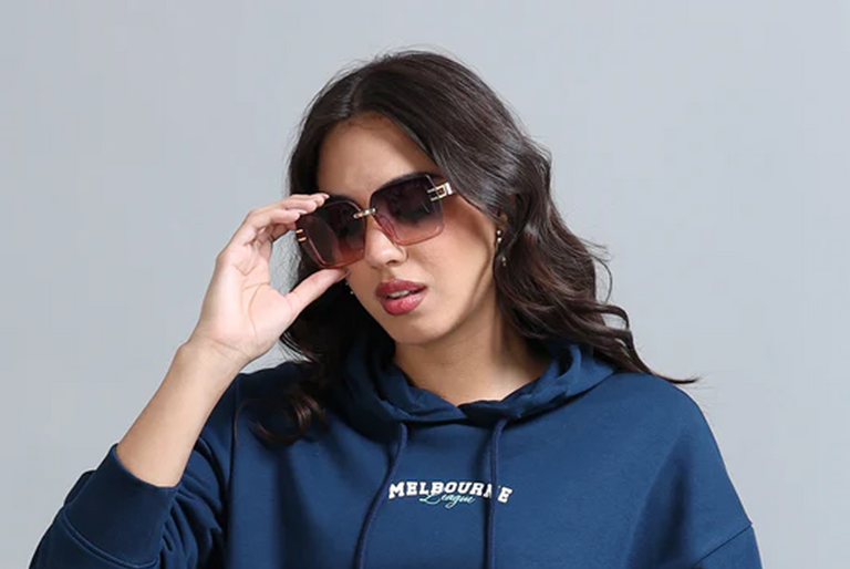 Woman wearing a navy blue hoodie with 'Melbourne' text, holding sunglasses against a gray background